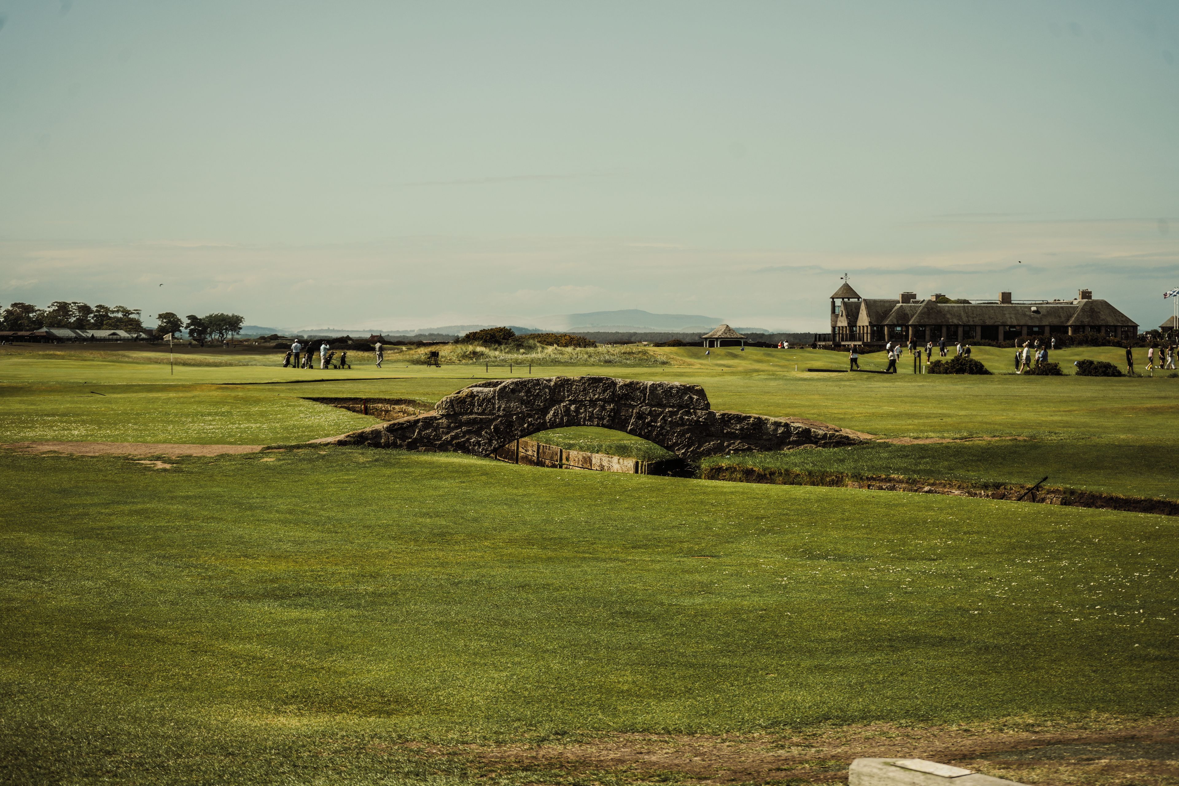 A golf course with a stone bridge, a clubhouse, and distant mountains.