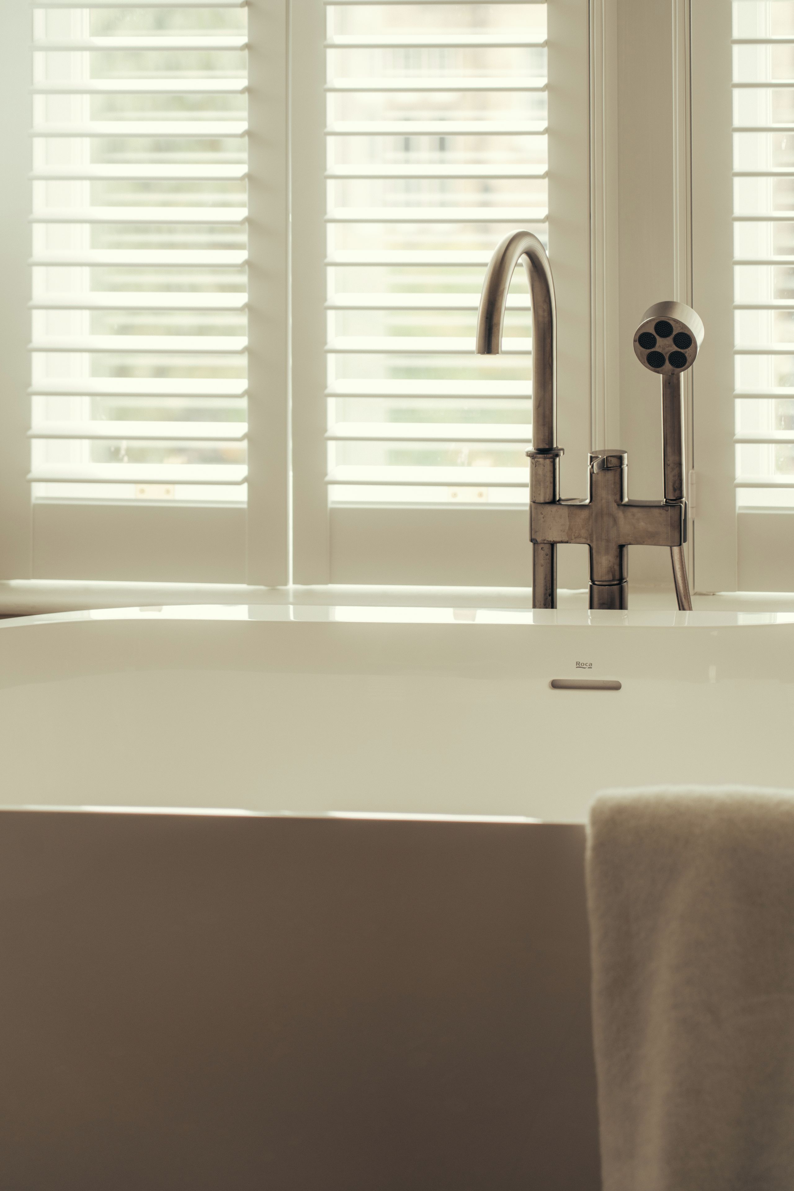A bathroom with a white sink, a modern faucet, and a window with blinds.