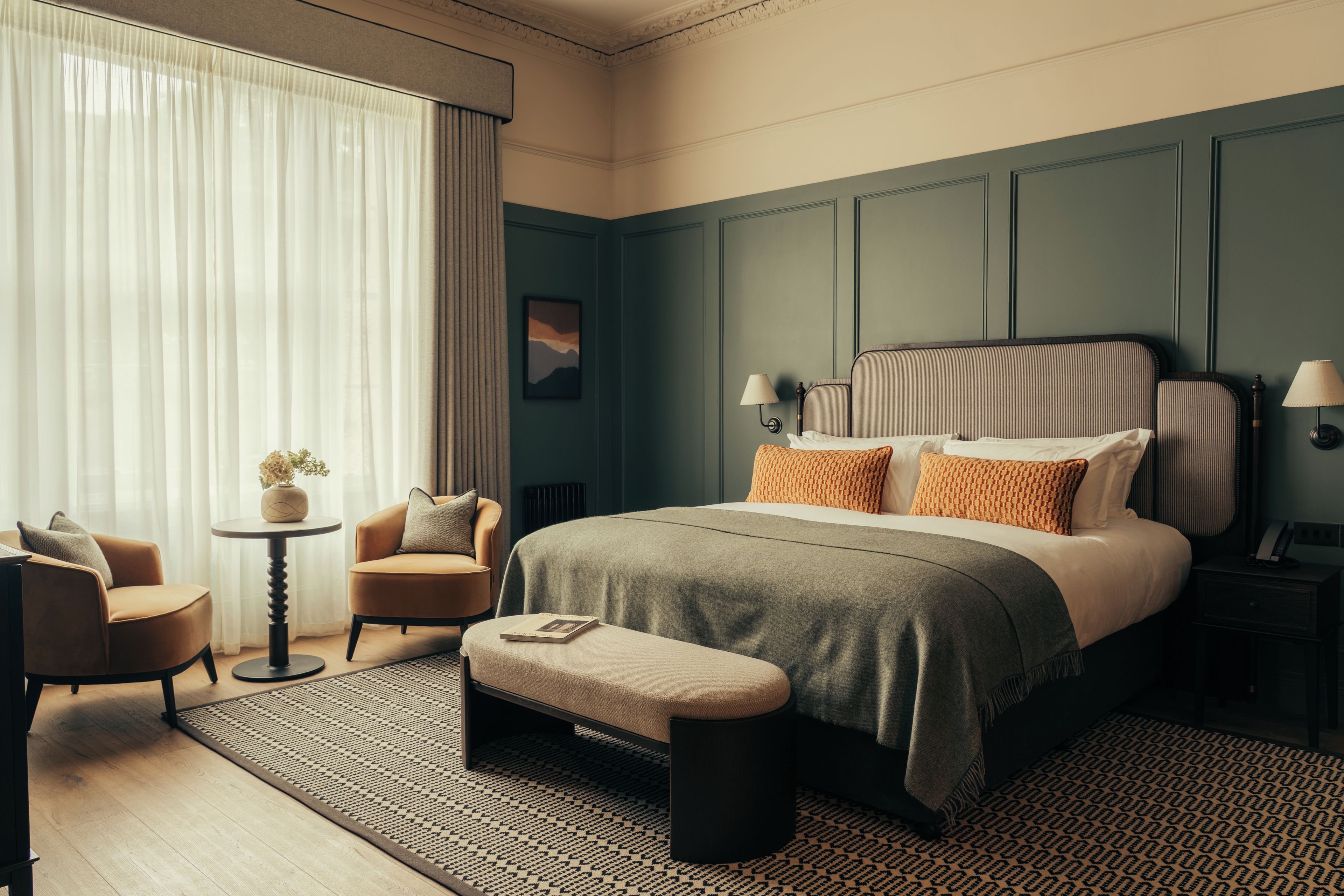 A hotel room with a large bed, a sitting area with a chair and a small table, and a large window with curtains.