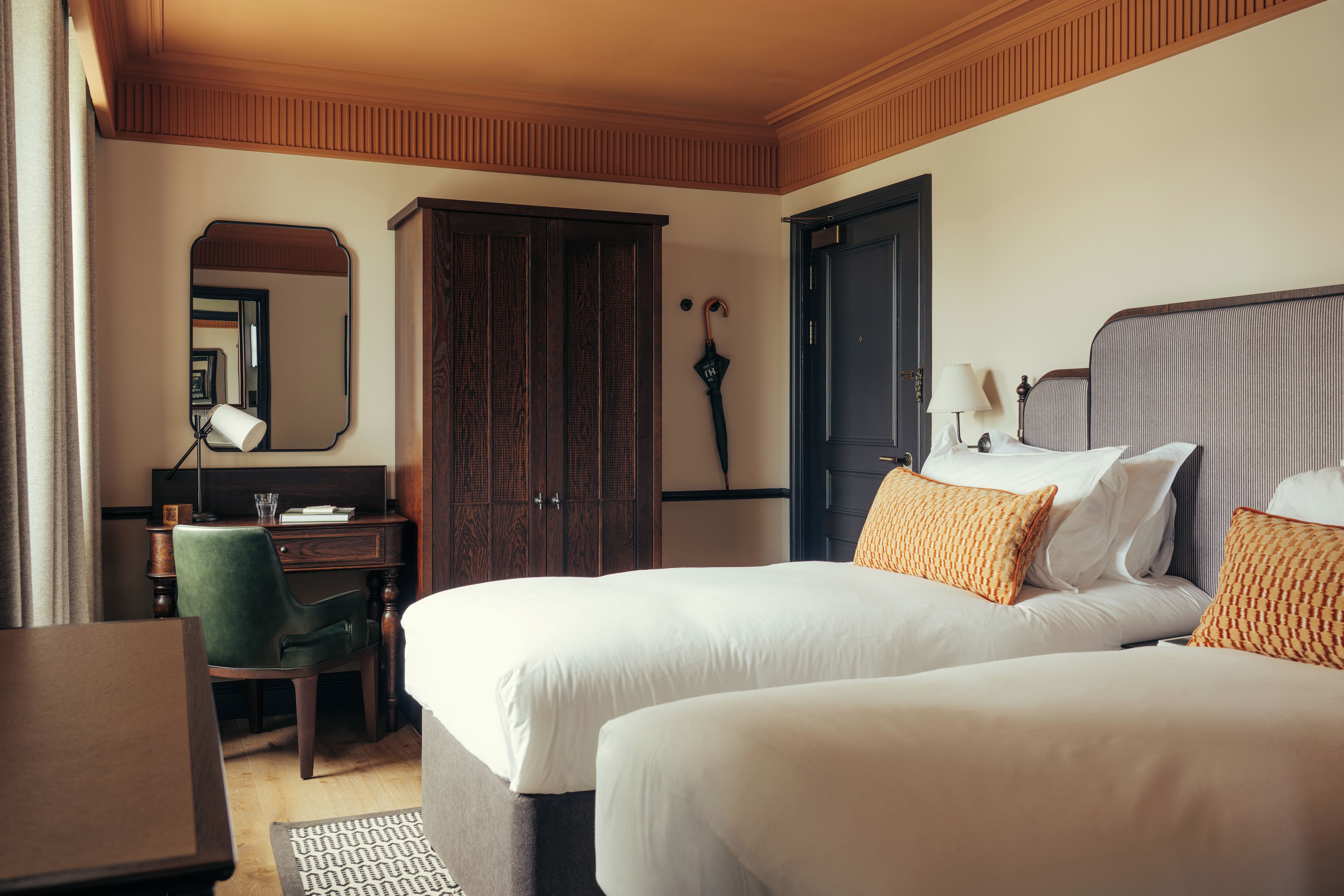 A hotel room with two beds, a desk, a chair, a wardrobe, and a mirror.