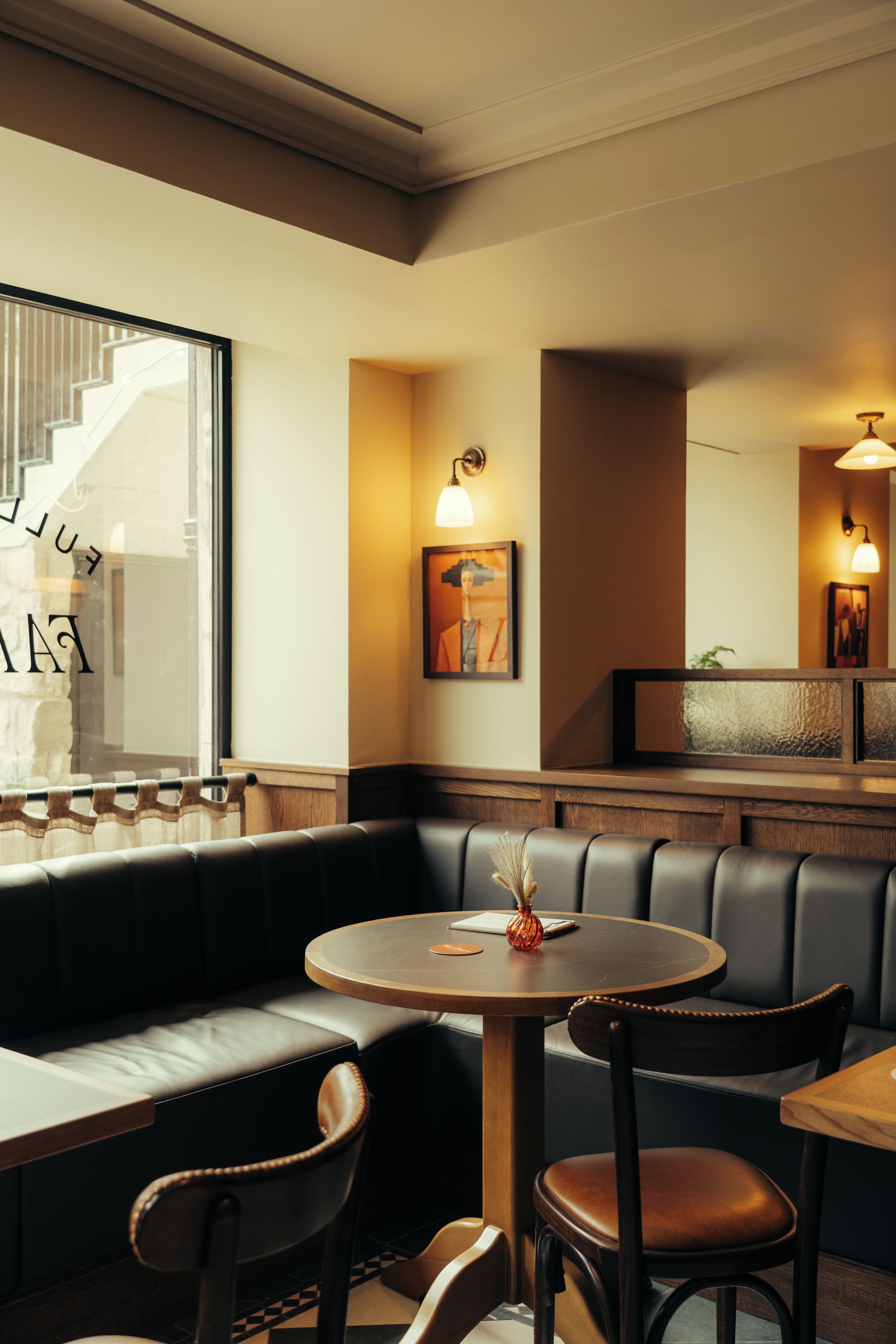 L’intérieur d’un restaurant, avec un espace aménagé en alcôves, une table ronde entourée de chaises et un escalier en arrière-plan.