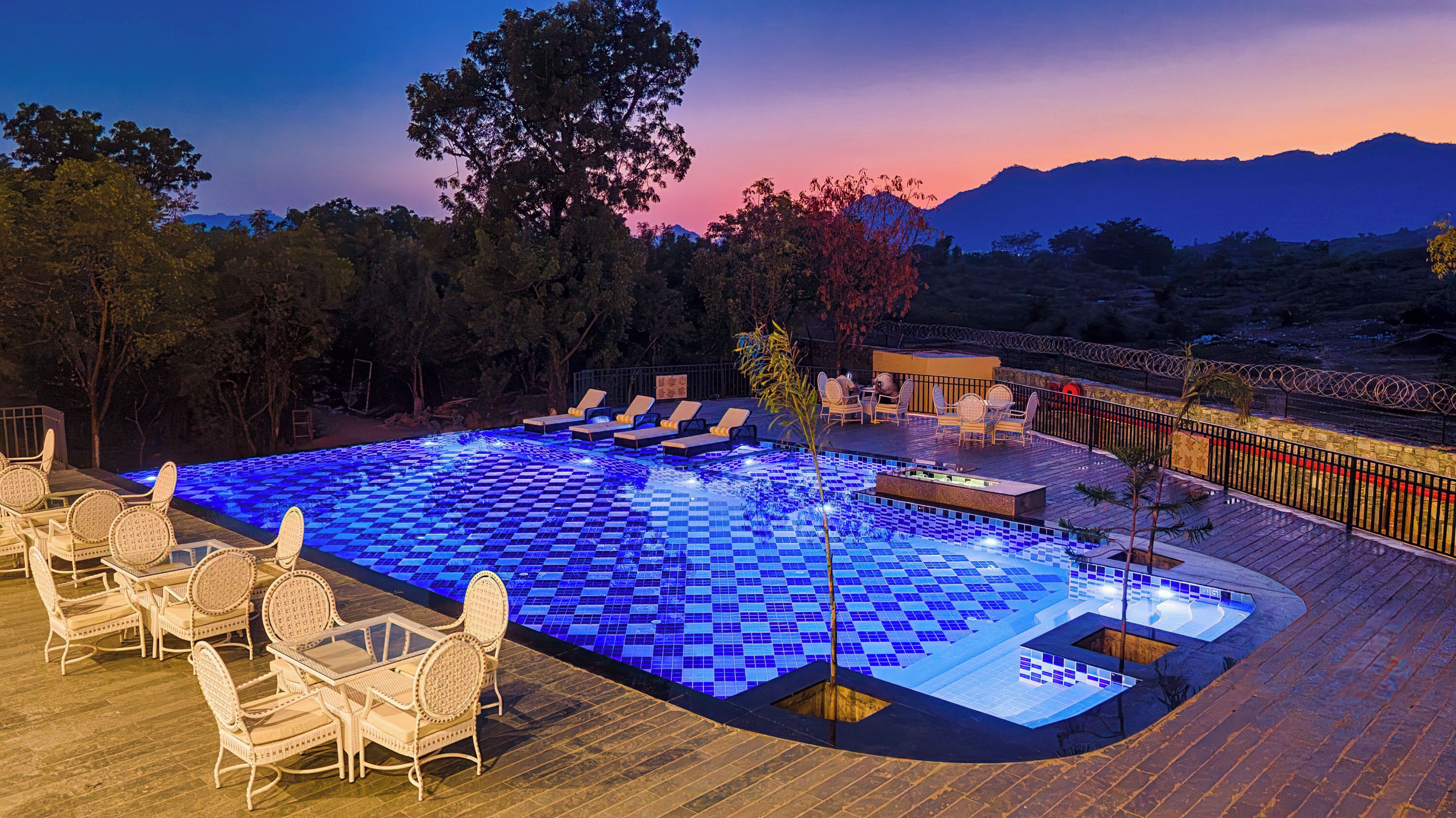 A pool with blue tiles, lounge chairs, and a deck area.
