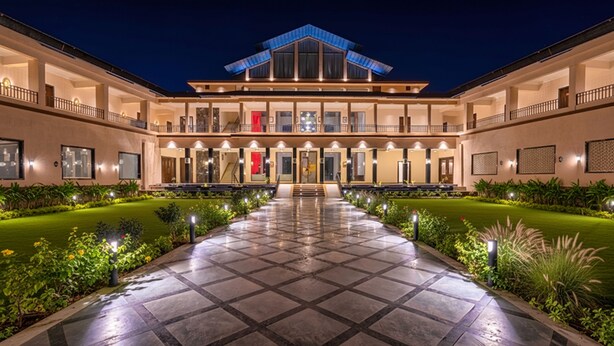 A large, modern hotel with a central courtyard, multiple balconies, and a well-lit entrance. - Amruthan Bagh Resort  (Udaipur)