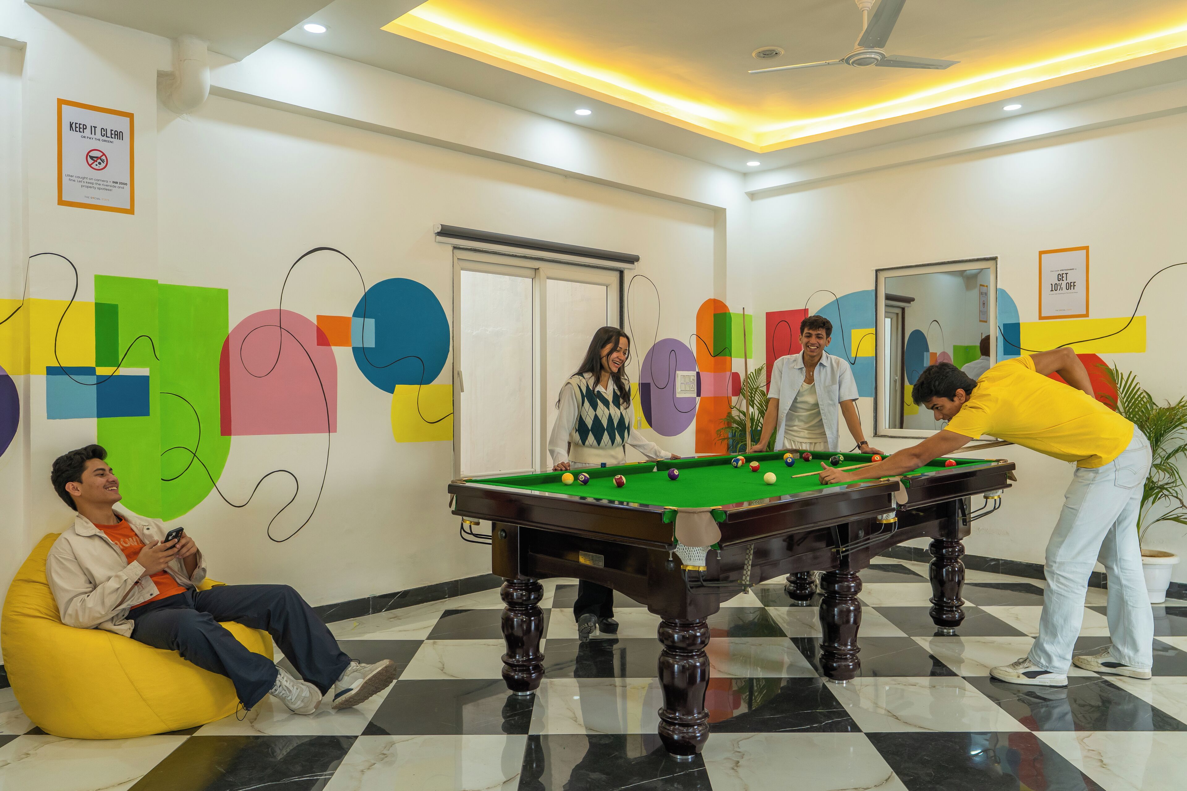 A pool table in a room with a checkered floor, a 'KEEP IT CLEAN' sign, and abstract wall art.