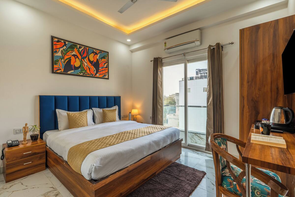 Quarto moderno com uma cama grande, uma mesa de cabeceira de madeira, uma escrivaninha com cadeira e vista para a cidade através de uma janela ampla.