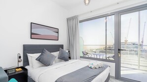 Een moderne hotelkamer met een groot bed, een nachtkastje, een digitale klok en uitzicht op de stad door grote ramen.