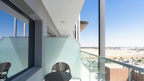 Een balkon met een glazen hekwerk, twee rieten stoelen en uitzicht op een woestijnlandschap.