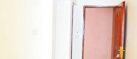 Un pasillo con una puerta de madera, una pared blanca con un símbolo y un cubo amarillo.