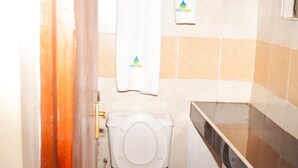 A small bathroom with a toilet, a towel hanging on the wall, and a shower area. - Mzedu Springs Hotel Mwatate (Taita Hills)