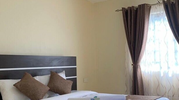 A neatly made bed with white and brown bedding, a dark headboard, and a brown throw blanket. - Mzedu Springs Hotel Mwatate (Taita Hills)