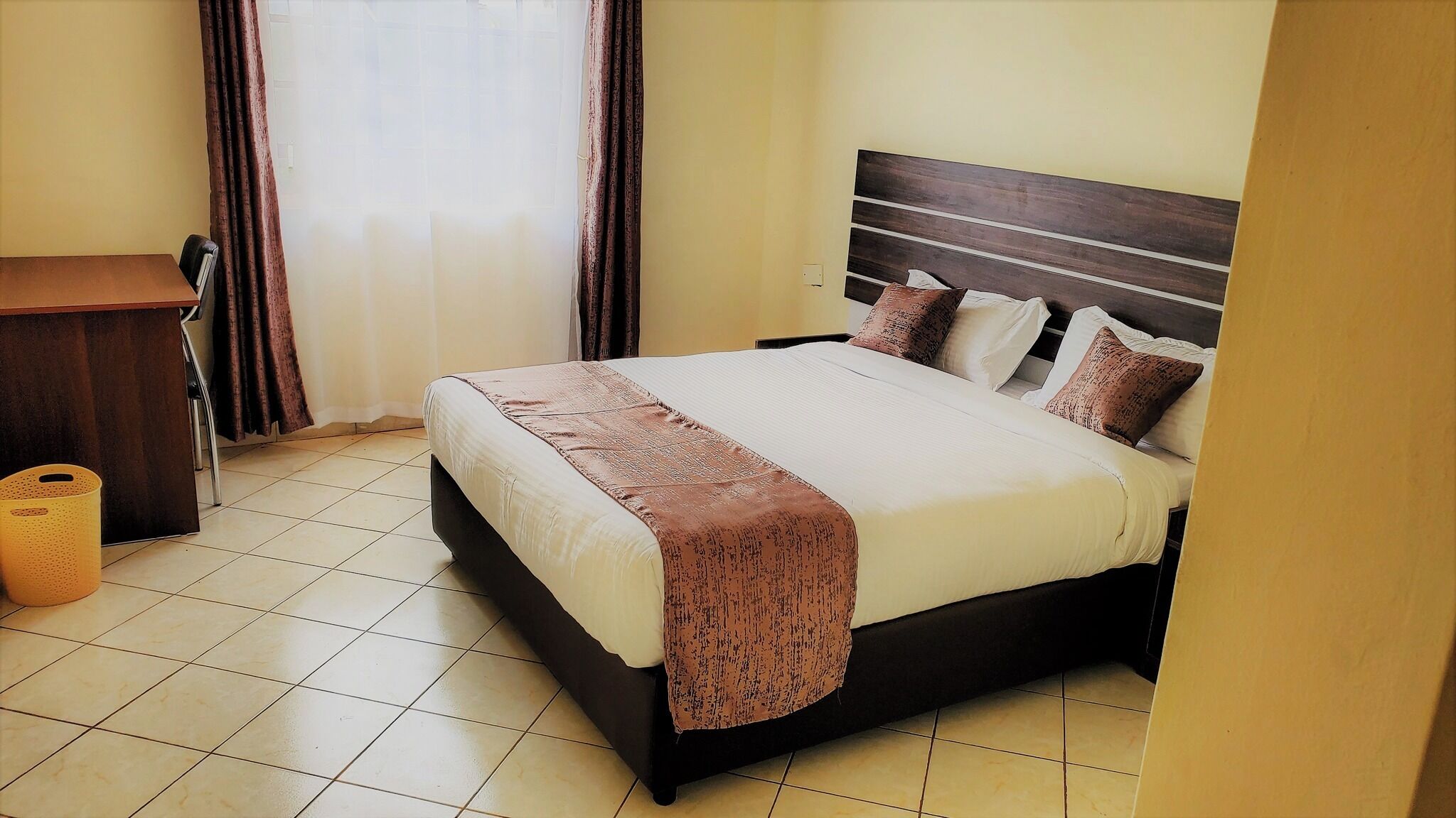 A hotel room with a bed, a desk, and a trash bin.