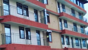 A multi-story building with balconies, parked vehicles, and a sign indicating a commercial space. - Mzedu Springs Hotel Mwatate (Taita Hills)