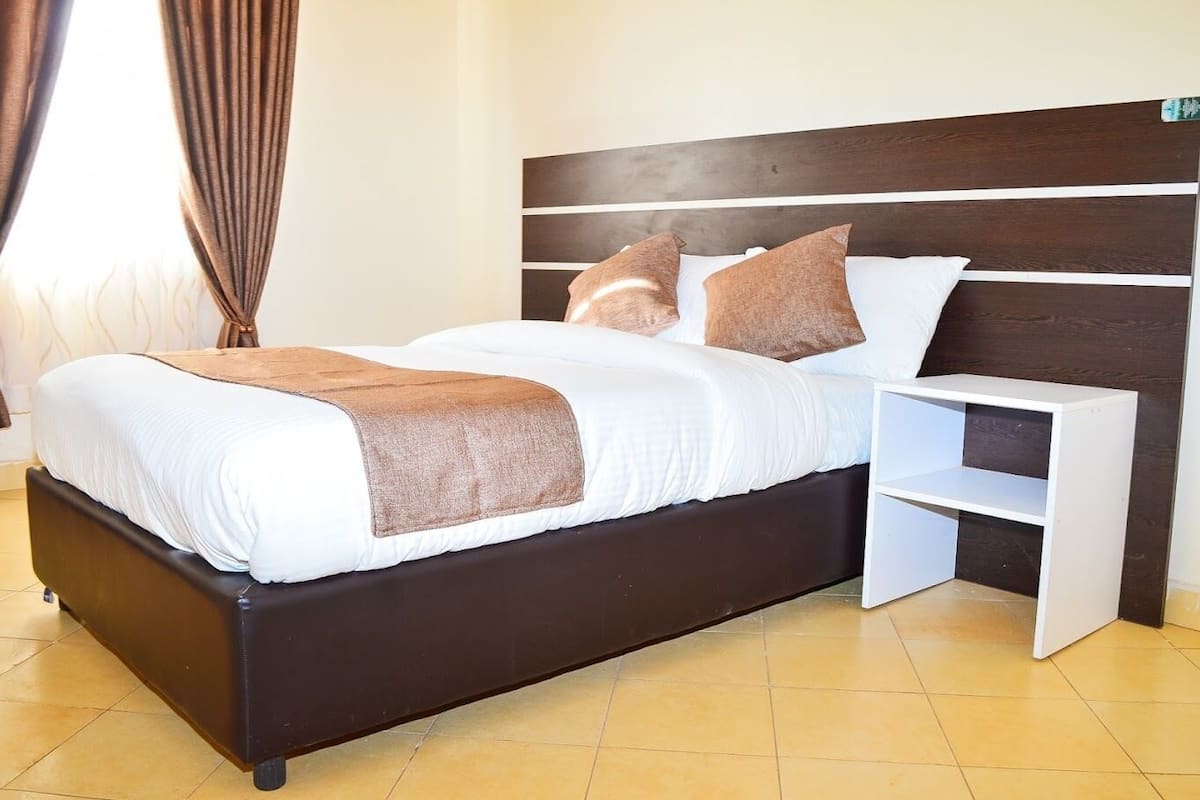 A modern bedroom with a dark wood headboard, white bedding, and a brown throw blanket.