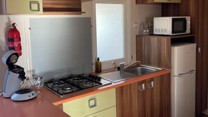 A compact kitchen with a gas stove, a microwave, a refrigerator, and wooden cabinets. - Mobile home with terrace and heated pool in the heart of the seaside resort (Port-la-Nouvelle)