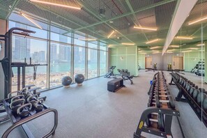 A gym with exercise equipment, large windows, and a city view. - Stylish 2 Bedroom with Panoramic canal View (Dubai)