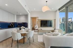 A modern living room with a dining area, a kitchen, and a large window with a city view. - Stylish 2 Bedroom with Panoramic canal View (Dubai)