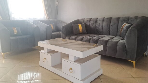 Ein Wohnzimmer mit einem grauen Sofa, einem weißen Couchtisch mit Schubladen und einem grauen Sessel.