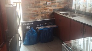 Eine Küche mit Holdelementen, einer Ziegelrückwand und einem Edelstahlspülbecken. Eine Waschmaschine und ein Tisch mit der Aufschrift "SMART-X 50" sind ebenfalls vorhanden.