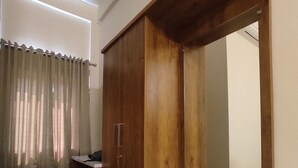 A bedroom with a wooden wardrobe, a large mirror, and a small bedside table. - Crown Town Hotel Kalamassery (Aluva)