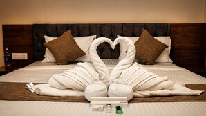A bed with a towel arrangement in the shape of a swan, a wooden headboard, and a brown throw blanket. - Crown Town Hotel Kalamassery (Aluva)