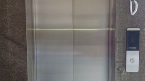 An elevator with a metallic finish, a control panel with a red emergency button, and a call button with a white handset. - Crown Town Hotel Kalamassery (Aluva)