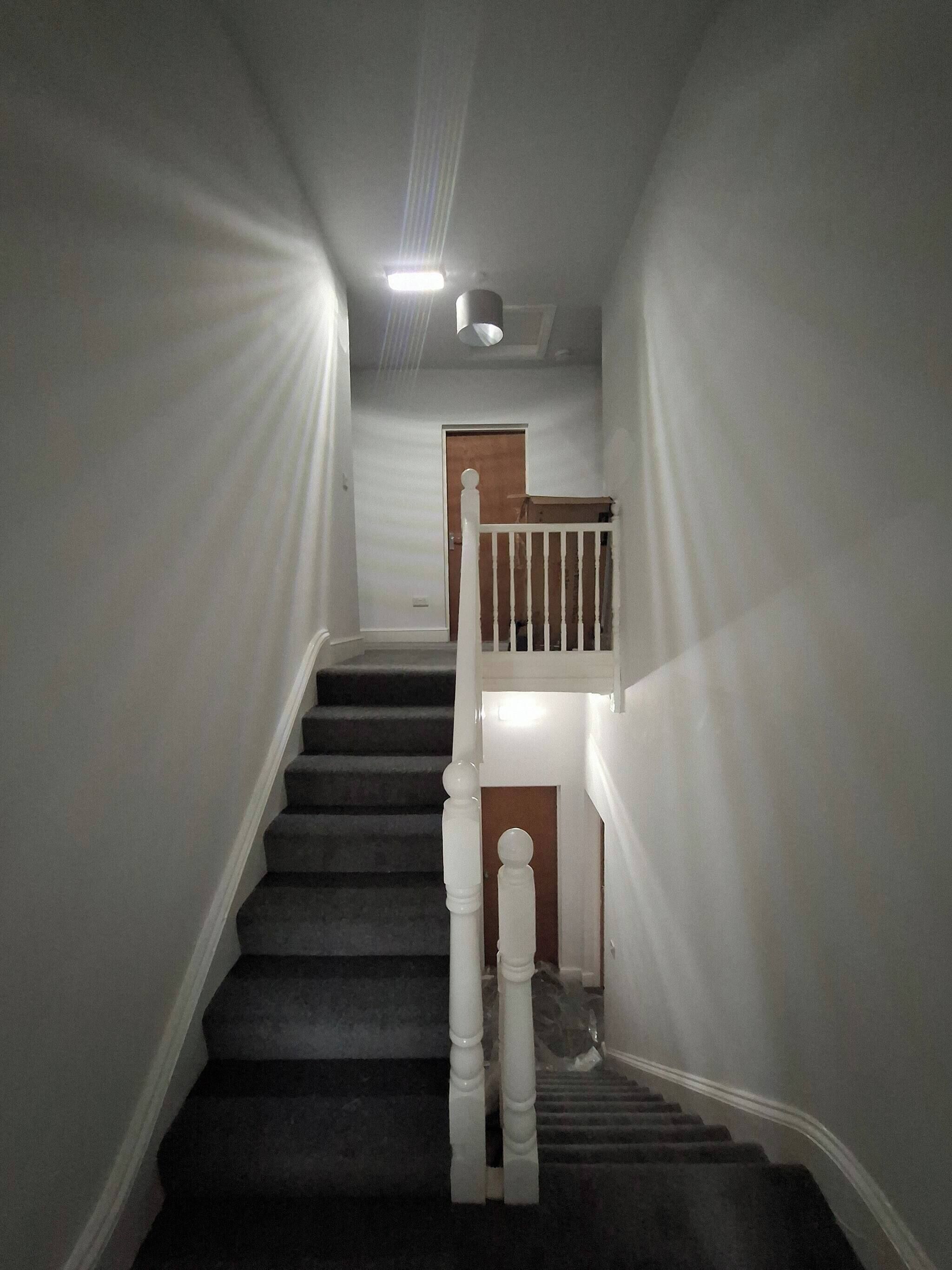 A staircase with white balusters and a wooden handrail, leading to a landing with a door.