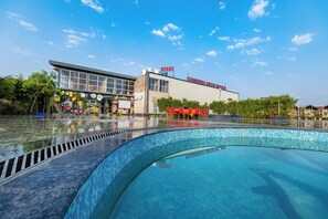 Una piscina con borde de azulejos, un edificio con un letrero que dice "Chandrika Green Resort" y una mesa roja con sillas al fondo.