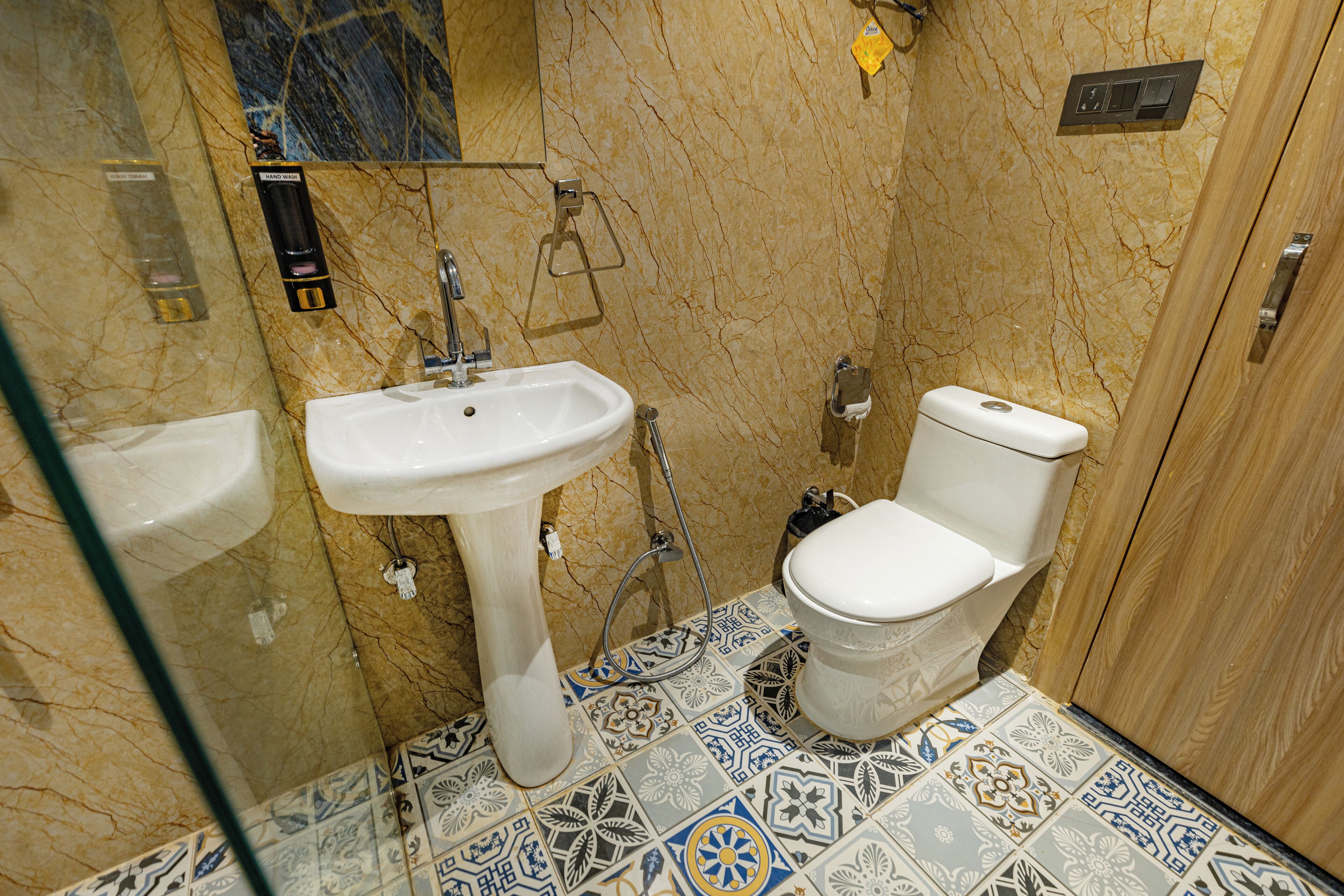 Een badkamer met een marmeren wand, een wastafel, toilet en vloertegels met een patroon.