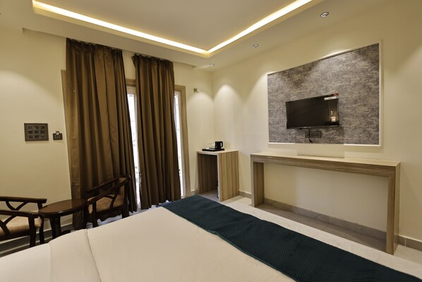 A hotel room with a bed, a TV mounted on the wall, a desk, and a chair. - Chandrika Greens Resort Near Prem Mandir (Vrindavan)