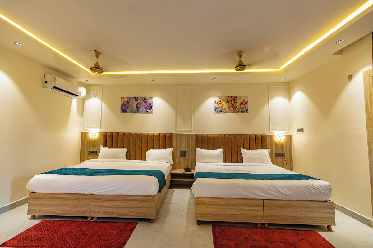 Une chambre d’hôtel avec deux lits, des têtes de lit en bois, un tapis rouge et un ventilateur de plafond.