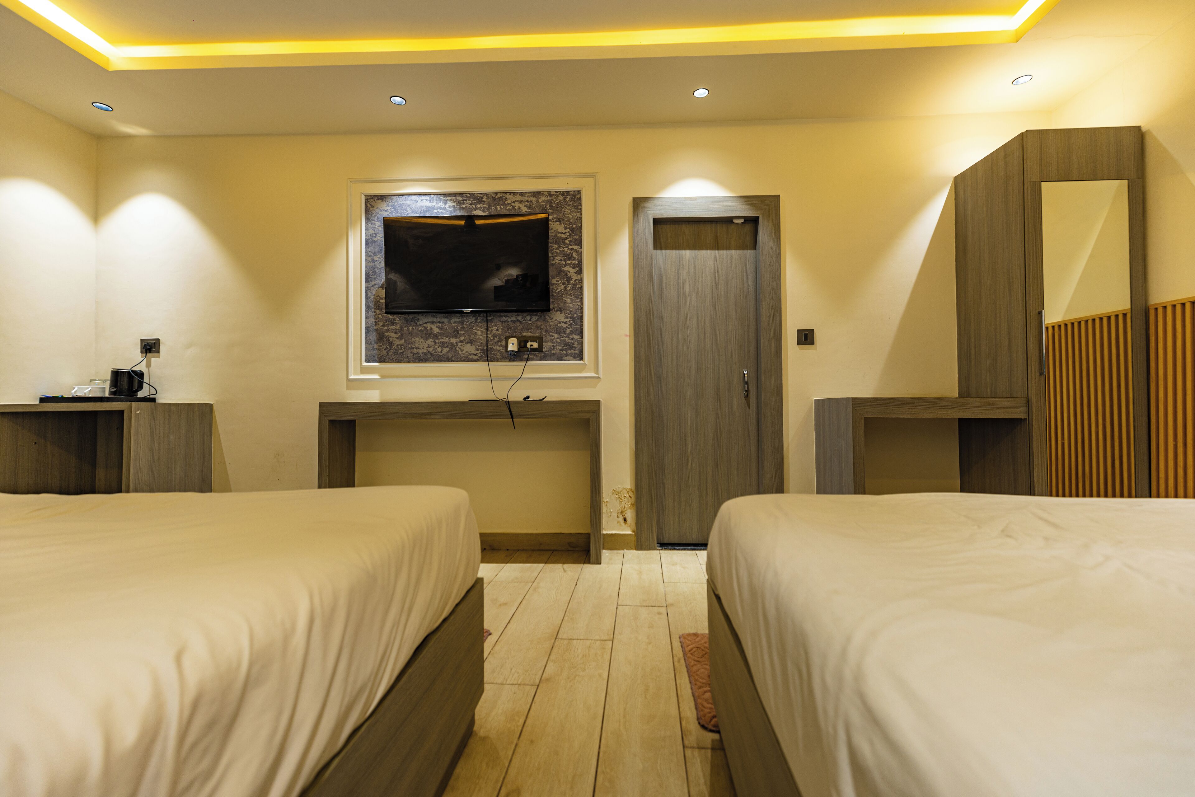 A hotel room with two beds, a TV mounted on the wall, a desk, and a wardrobe.