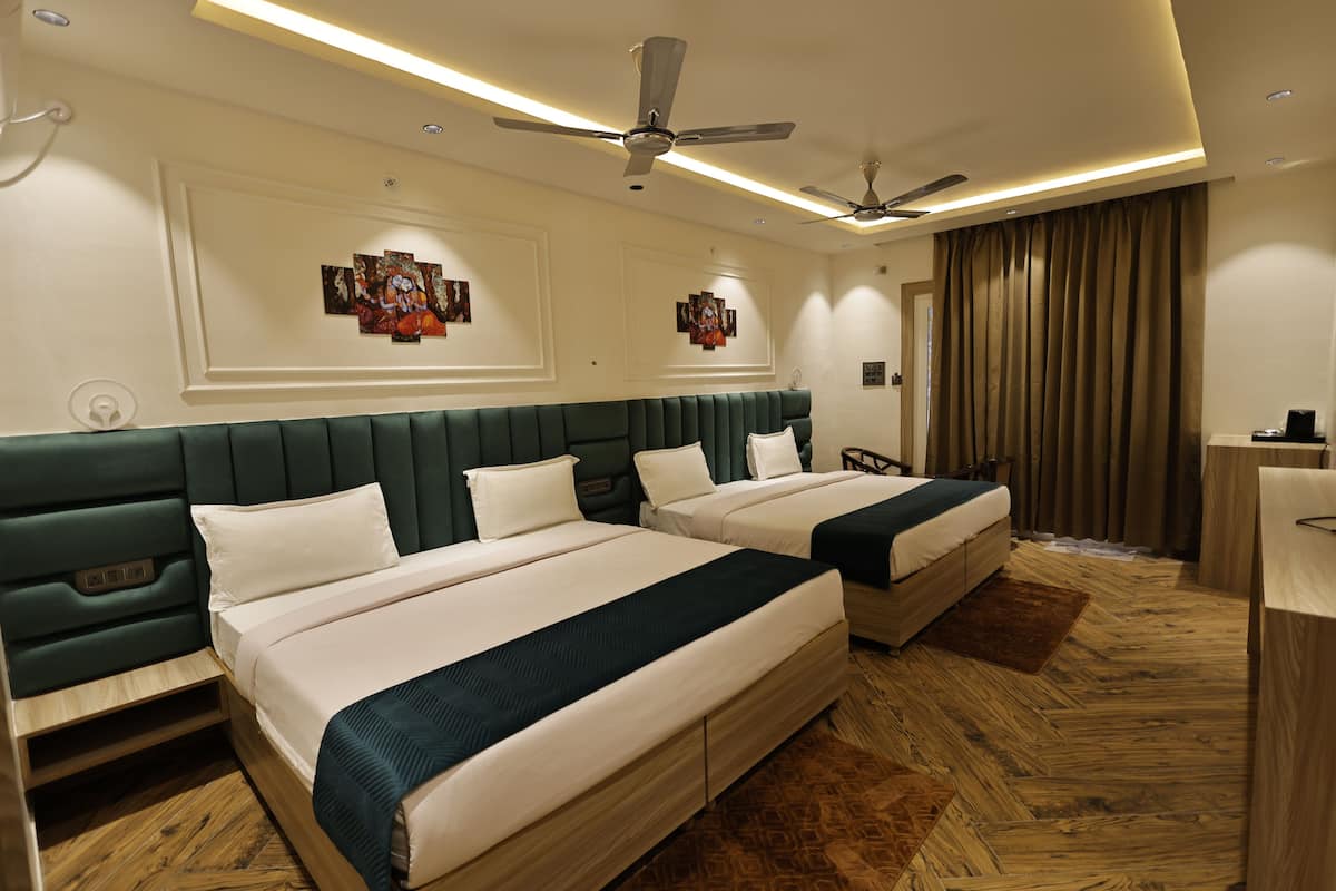 Une chambre d’hôtel avec deux lits, une tête de lit recouverte d’un tissu vert, un plancher en bois, des ventilateurs de plafond, un éclairage encastré et des œuvres d’art accrochées aux murs.