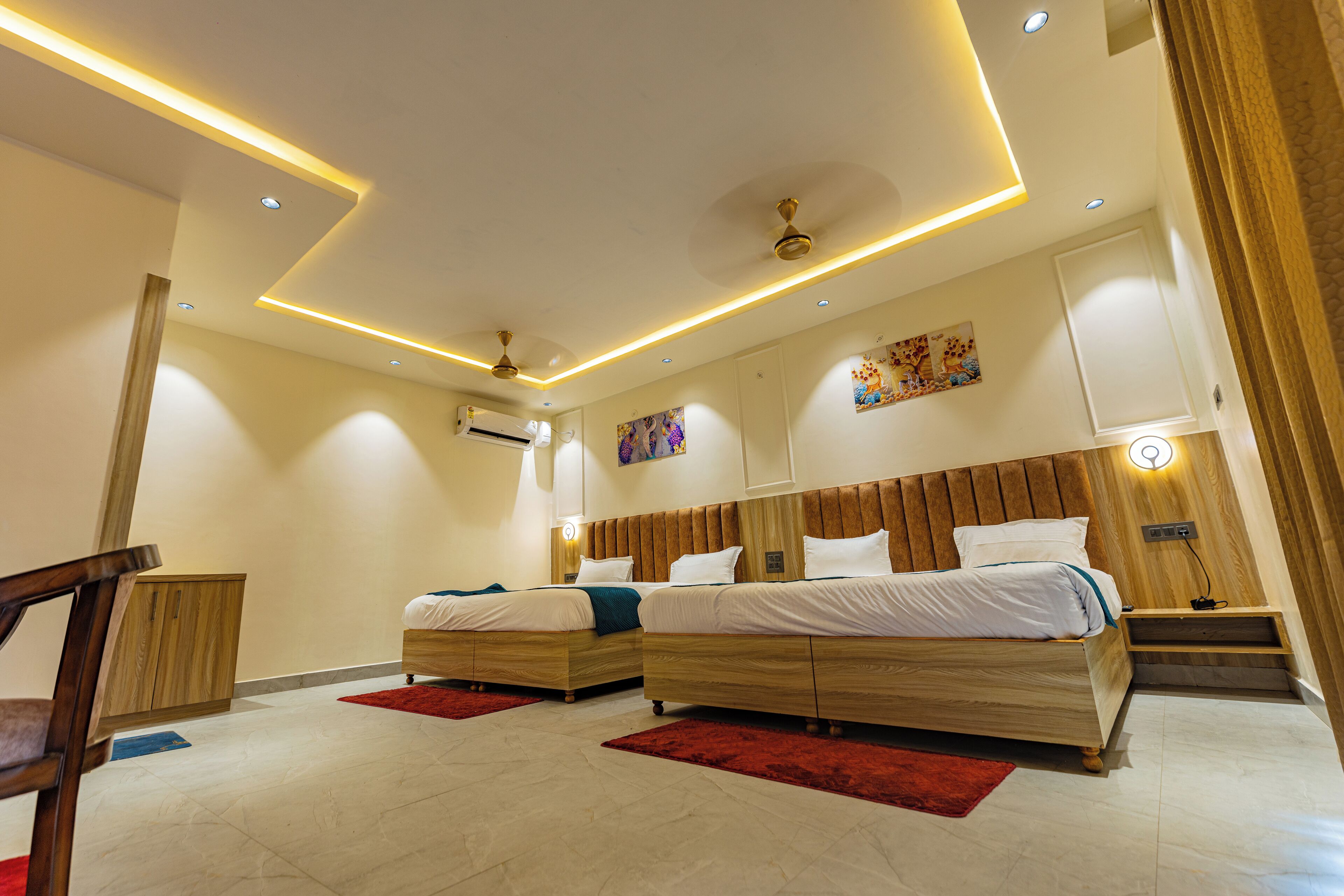 A modern bedroom with two beds, a wooden headboard, recessed ceiling lighting, and a red rug.