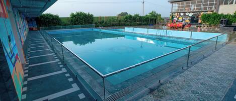 A swimming pool with a glass edge, surrounded by a tiled walkway and a covered area with a mural.