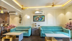 Een moderne woonkamer met blauwgroene banken, marmeren bijzettafels en een plafondventilator.