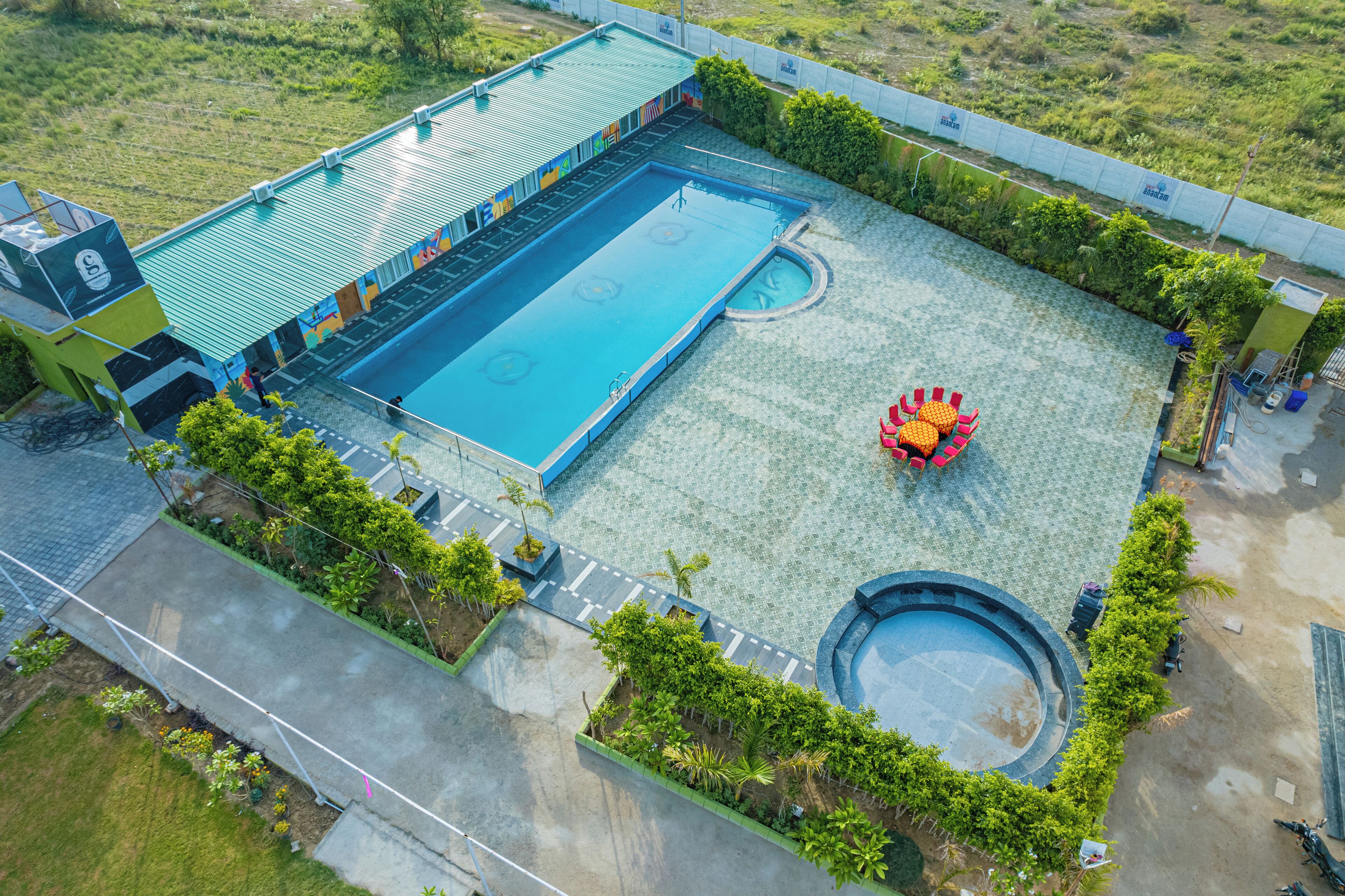 An aerial view of a swimming pool complex with a large pool, a smaller circular pool, and a covered area with a roof.