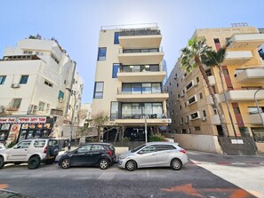 A multi-story building with balconies, a street food restaurant, and parked cars. - MAMAD Modern&Bright with Balcony in City Center by FeelHome (Tel Aviv - Jaffa)