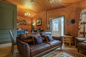 A cozy living room with a brown leather sofa, a wooden ceiling, and a brick wall. - Pools Cottage 14-Stable House Warwickshire Escape (Kenilworth)