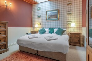 A neatly made bed with white linens, two bedside lamps, and a plaid-patterned wall with framed pictures. - Pools Cottage 14-Stable House Warwickshire Escape (Kenilworth)