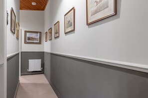 A hallway with framed pictures on the wall, a radiator, and a carpeted floor. - Pools Cottage 14-Stable House Warwickshire Escape (Kenilworth)
