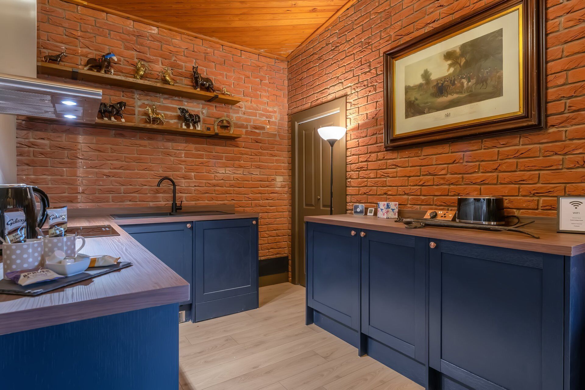 A kitchen with brick walls, wooden ceiling, and a framed painting.