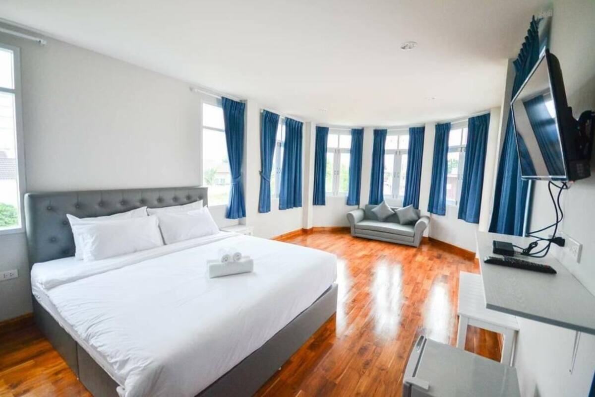 Une chambre avec un grand lit, un canapé gris, une télévision et un bureau.