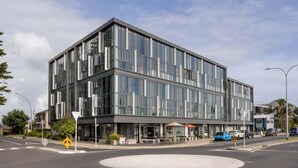 A modern building with large windows and a flat roof, located at a street corner with a roundabout. - Tree Tops Loft - Stylish, Private 2-Bedroom Retreat in Mount Maunganui (Mount Maunganui)