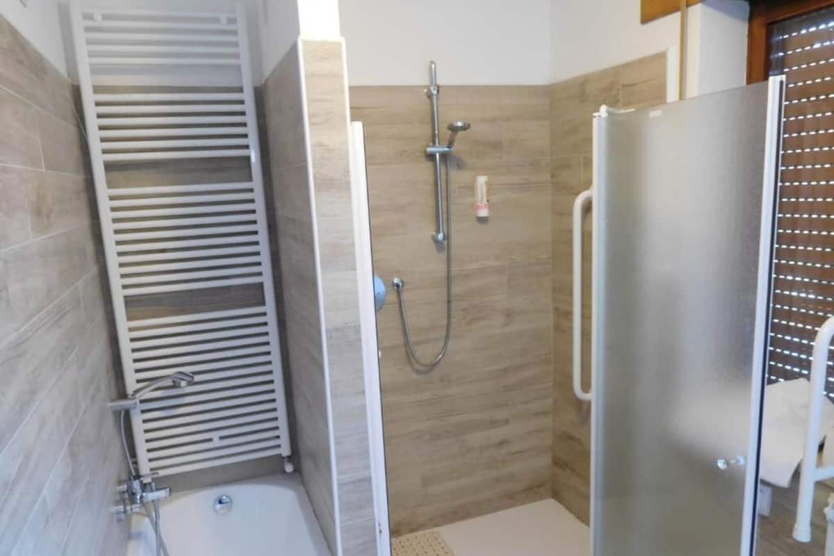 A shower area with a glass door, a white towel rack, and a showerhead.