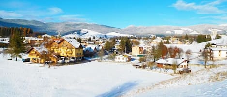 Un pueblo cubierto de nieve con edificios tradicionales, cielo despejado y montañas al fondo.