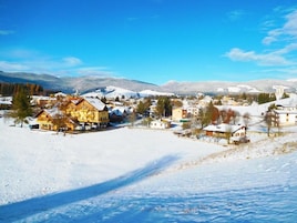 Un pueblo cubierto de nieve con edificios tradicionales, cielo despejado y montañas al fondo.