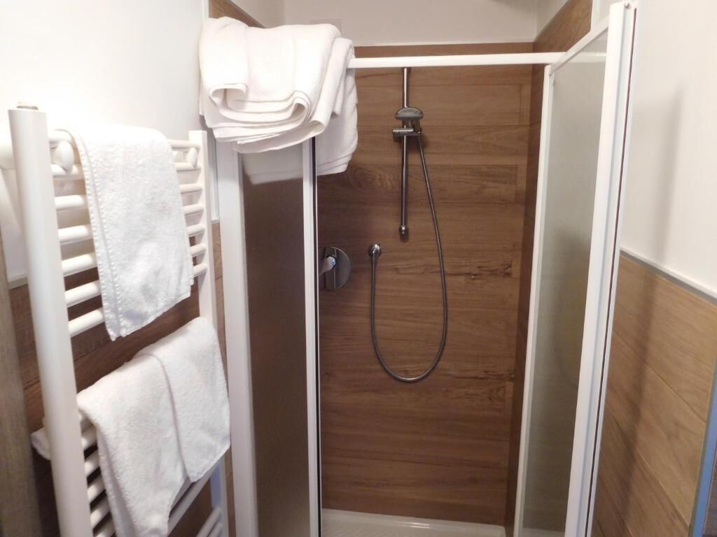 Un área de ducha con pared de madera, toallero blanco y ducha.