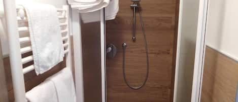 A shower area with a wooden wall, a white towel rack, and a showerhead.