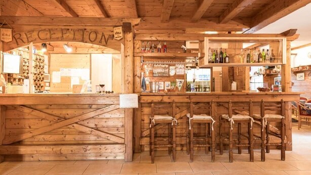 A wooden reception area with a sign reading "RECEPTION," a bar with stools, and shelves stocked with bottles and glasses. - Hotel Vescovi (Asiago)