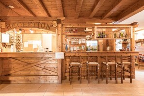 A wooden reception area with a sign reading "RECEPTION," a bar with stools, and shelves stocked with bottles and glasses. - Hotel Vescovi (Asiago)